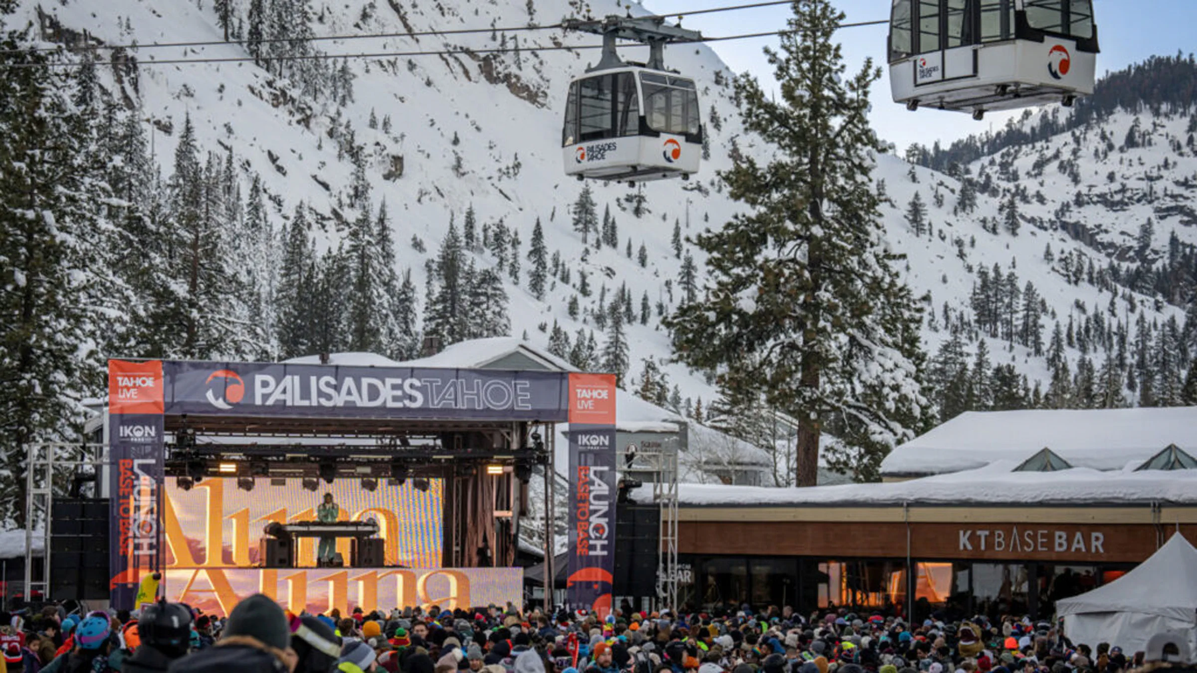 A live outdoor concert at Palisades Tahoe with a large crowd, snowy mountains in the distance, and two gondola cars in the sky.